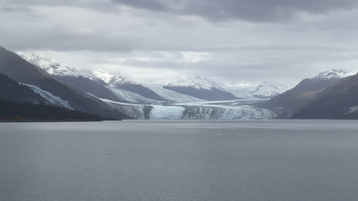 A glacier across gray water between dark mountain slopes
